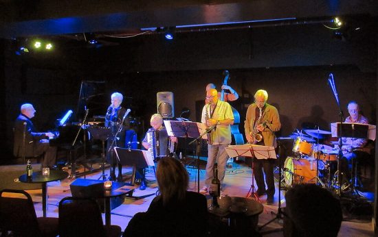Mike Westbrook Band v Cafe Posk, Hammersmith. Mike Westbrook (piano), Kate Westbrook (zpěv), Karen Street (akordeon), Pete Whyman (saxofon), Chris Biscoe (saxofon), Marcus Vergette (kontrabas) a Coach York (bicí). (2. 12. 2023) (Credit photo: AndyScott, Wikimedia, Creative Commons Zero, Public Domain Dedication)